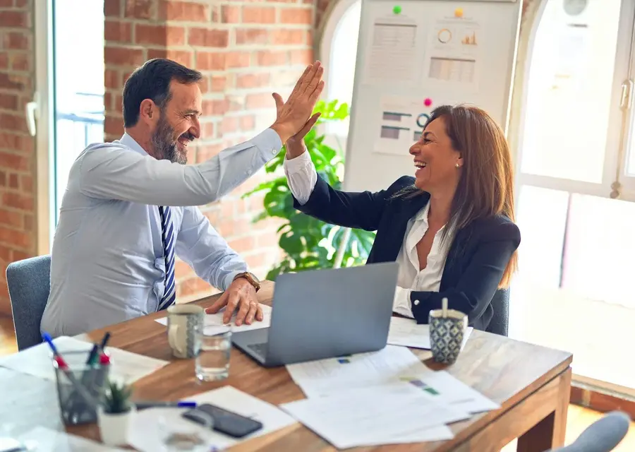 Two business colleagues high-fiving across a desk after a successful meeting
